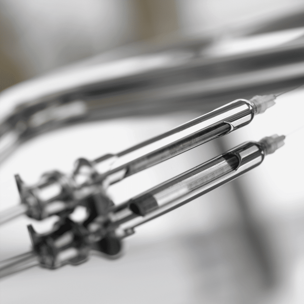 Close-up of two metallic dental syringes with reflective surfaces, set against a blurred background in a clinical or medical setting.